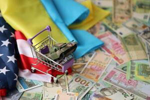 Toy tank on US flag and ukrainian flag on many banknotes of different currency photo