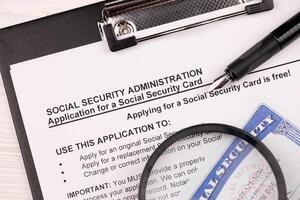 United States social security number cards lies on Application from social security administration on A4 tablet lies on office table with pen and magnifying glass photo