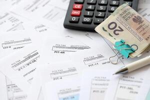 Polish zloty money PLN, calculator and pen on big amount of polish PIT, CIT and VAT tax forms close up. Accounting, bureaucracy and taxpayers routine photo