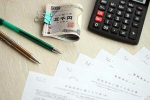 Japanese tax forms lies on table with calculator, pen and japanese yen money bills roll photo