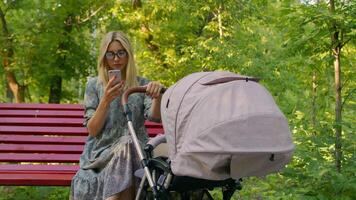A Young Mother In A Summer Dress Is Sitting On A Red Bench Looking At The Phone photo