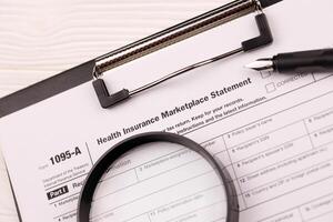 IRS Form 1095-A Health Insurance Marketplace Statement tax blank on A4 tablet lies on office table with pen and magnifying glass photo