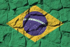 Brazil flag depicted in paint colors on old stone wall closeup. Textured banner on rock wall background photo