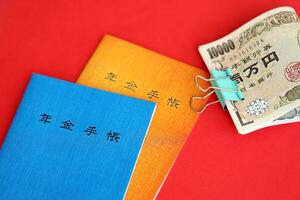Japanese pension insurance booklets on table with yen money bills. Blue and orange books photo