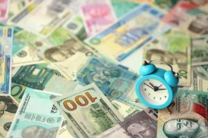 Small alarm clock on many banknotes of different currency. Background of time and money photo