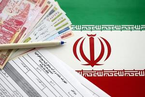 Iranian annual income tax return form F20-25-006 ready to fill on table with pen and iranian money on flag photo