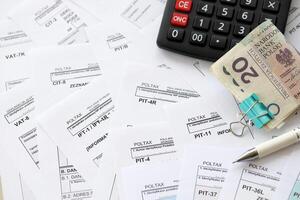 Polish zloty money PLN, calculator and pen on big amount of polish PIT, CIT and VAT tax forms close up. Accounting, bureaucracy and taxpayers routine photo