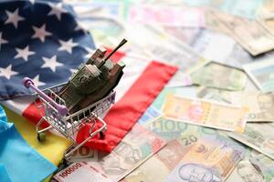 Toy tank on US flag and ukrainian flag on many banknotes of different currency photo