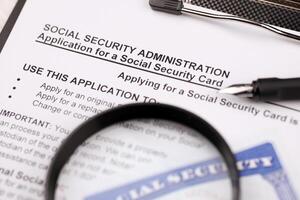 United States social security number cards lies on Application from social security administration on A4 tablet lies on office table with pen and magnifying glass photo