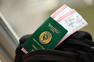 Green Nigerian passport with airline tickets on touristic backpack photo