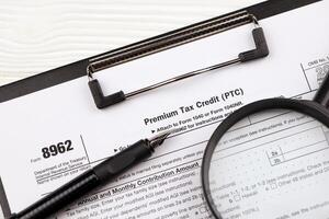 IRS Form 8962 Premium tax cerdit PTC blank on A4 tablet lies on office table with pen and magnifying glass photo