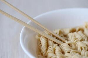 Bowl of instant cooking noodles with wooden chopsticks on white wooden table photo