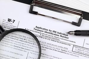 IRS Form W-7 Application for IRS Individual taxpayer identification number blank on A4 tablet lies on office table with pen and magnifying glass photo