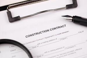 Construction contract form on A4 tablet lies on office table with pen and magnifying glass photo