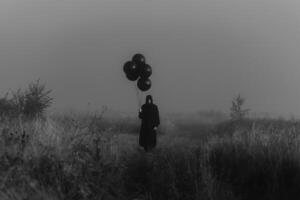 scary dark man in a monster costume with a hood with balloons in his hand photo