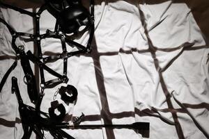 set of sex toys on the background of a white sheet in bed. Leather whip, handcuffs and mask photo