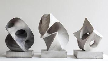 Three sculptures made of concrete, one of which is a cube. The sculptures are placed on a white surface photo