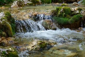 Crystal-clear water of a mountain stream flowing over mossy rocks photo