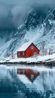 A red house sits on a snowy mountain. The house is surrounded by a beautiful lake and mountains photo