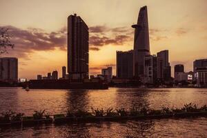 Sunset view of Bitexco Tower, buildings, roads, Bason bridge and Saigon river in Ho Chi Minh city, container cargo ship on Saigon river. Travel concept. photo