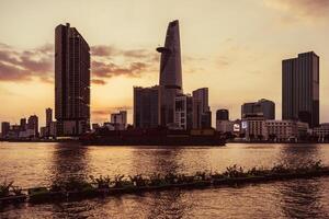 Sunset view of Bitexco Tower, buildings, roads, Bason bridge and Saigon river in Ho Chi Minh city, container cargo ship on Saigon river. Travel concept. photo