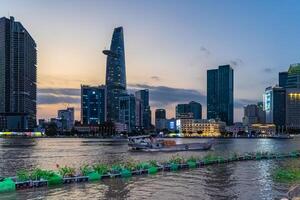 Sunset view of Bitexco Tower, buildings, roads, Bason bridge and Saigon river in Ho Chi Minh city, container cargo ship on Saigon river. Travel concept. photo