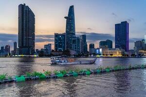 Sunset view of Bitexco Tower, buildings, roads, Bason bridge and Saigon river in Ho Chi Minh city, container cargo ship on Saigon river. Travel concept. photo