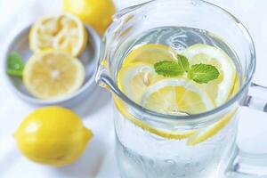 Clear water in a glass pitcher with slices of lemon and mint leaves photo
