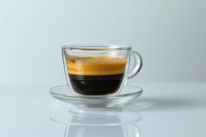 A cup of coffee with a glass saucer sits on a table. The coffee is dark and frothy, with a rich aroma. The cup is almost empty, with only a small amount of coffee left in it photo