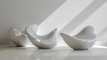 Three white chairs are arranged in a room with a white wall. The chairs are all different shapes and sizes, but they all have a similar design. The room is very clean and simple photo