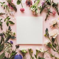 Square blank card surrounded by pastel colored flowers on a light pink background in a top view photo