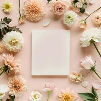 Square blank card surrounded by pastel colored flowers on a light pink background in a top view photo