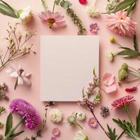 Square blank card surrounded by pastel colored flowers on a light pink background in a top view photo