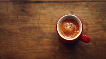 A red coffee cup with a white lid sits on a wooden table. The coffee is steaming and the cup is almost empty photo