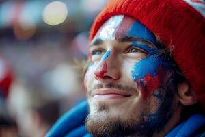 A joyful French man with his face painted in the blue white and red colors of the France flag, cheering at a football match, with a blurred stadium background. photo
