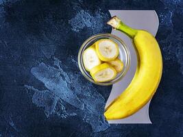 Ripe fresh yellow banana with sliced pieces in a bowl on a textured blue background with copy space photo