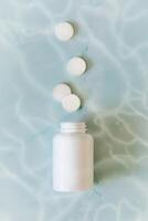 White pills and white bottle with copy space on blue water background photo