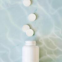 White pills and white bottle with copy space on blue water background photo