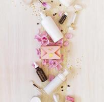 Romantic still life with cosmetics bottles, accessories, a gift box and rose petals on white background photo