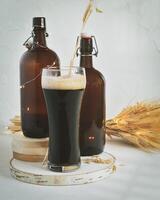 Glass of dark, unfiltered beer, two dark brown bottles and bouquet of wheat on a white background photo