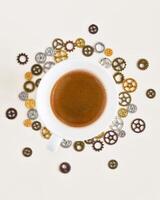 A cup of freshly brewed espresso around gears and cogs on a white background photo