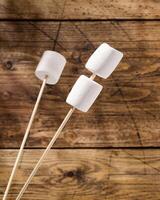 White marshmallow on wooden sticks and shade from palm leaves on a woodenbackground photo