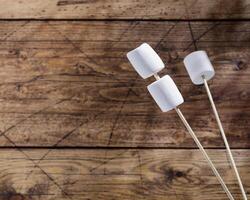 White marshmallow on wooden sticks and shade from palm leaves on a woodenbackground photo