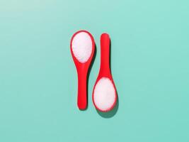 Red plastic spoons with sea salt and sugar on a blue background photo