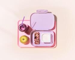 lunch box with yogurt, cereal bar, apple and oatmeal berries cocktail on a pink background photo