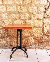 A wrought-iron table is not set against the background of a beautiful textured old wall made of large stone and decorated with wine bottles on a narrow street of the old European city photo