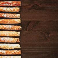 Waffle tubes with powdered sugar on a wooden background with copy space photo