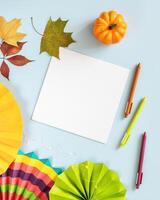 White sheet of paper, colorful paper fans, pens and autumn decorations on a blue background photo