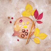 A wooden tray with dry leaves, watercolors, brushes, cranberries and chestnuts photo