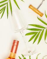 Empty wine glass, bottle of rose wine and palm leaves photo